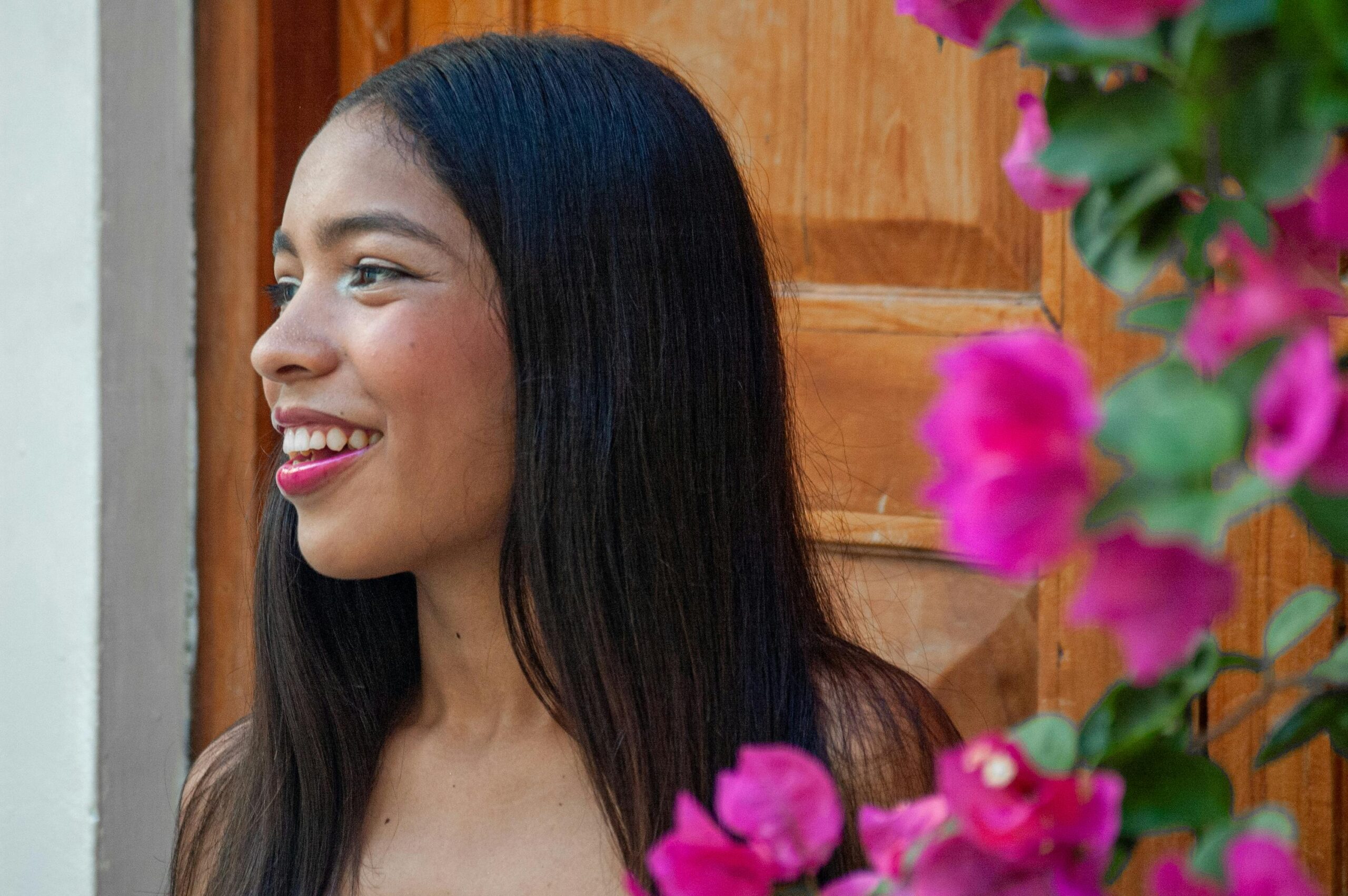 Profil einer lächelnden jungen Frau mit leuchtend rosa Blumen im Vordergrund.